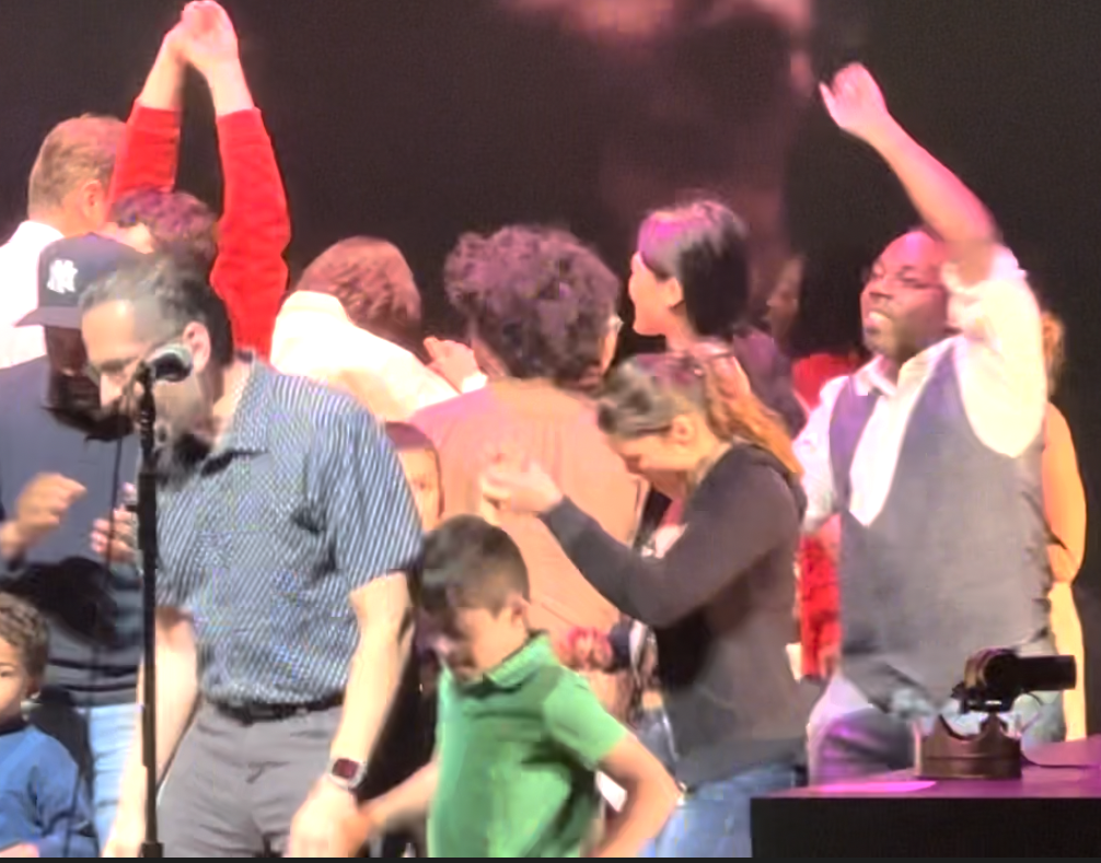 People are dancing on a stage, and the shot is blurred because of their joyful movement. 