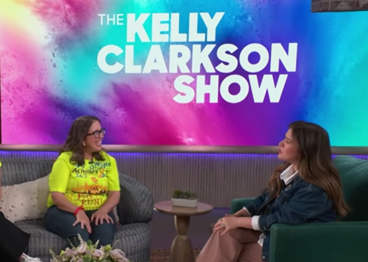 Sara wears a bright yellow shirt and sits on a couch on the Kelly Clarkson set, talking to the singer. 