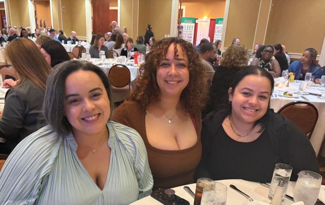 Sara, Karina, and Yismel smile while sitting at a table. 