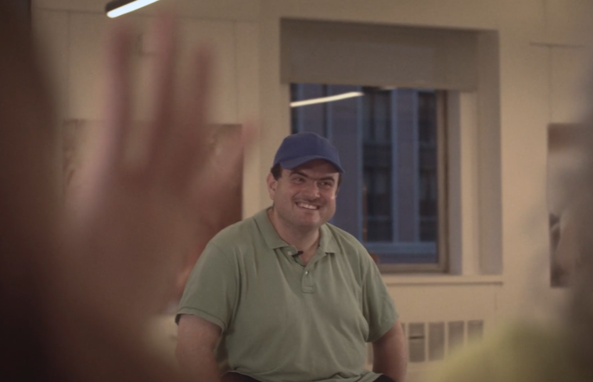 Oscar is seen in a still from the video wearing a light green shirt and a ballcap. 