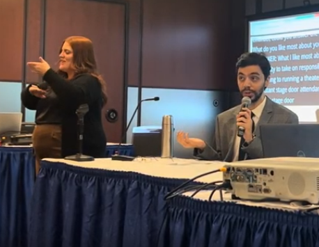 Emanuel holds a mic while sitting at a table with a blue ruffle.