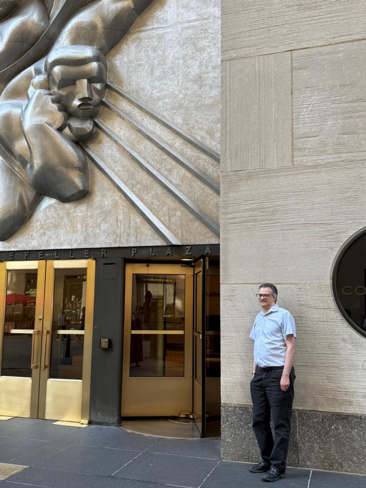 Ben stands outside 50 Rockefeller Plaza with the iconic art deco stylings on the exterior of the building.