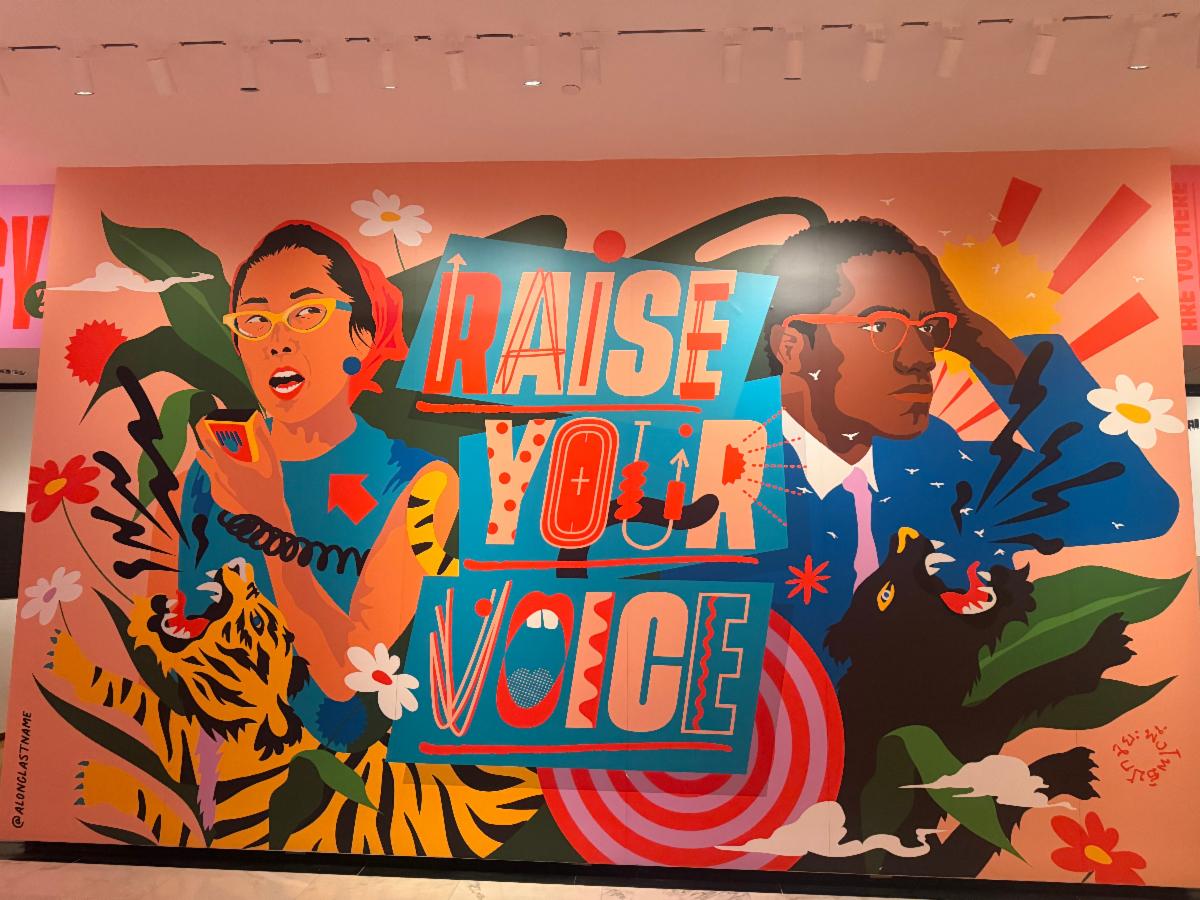 A brightly colored mural has the words "Raise your Voice." 