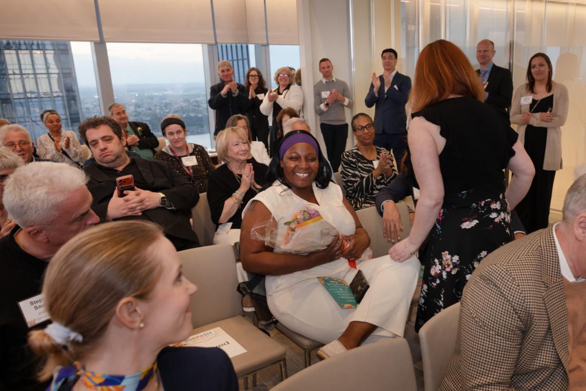 Tamesha, seated in an audience, is smiling after being handed a bouquet of flowers. 