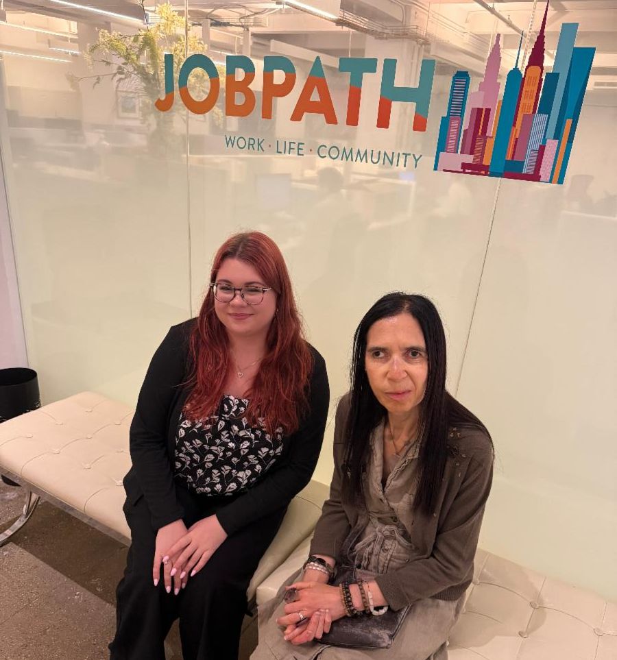 Kat and Shawn sit on a white bench outside the Job Path office, under the logo. 