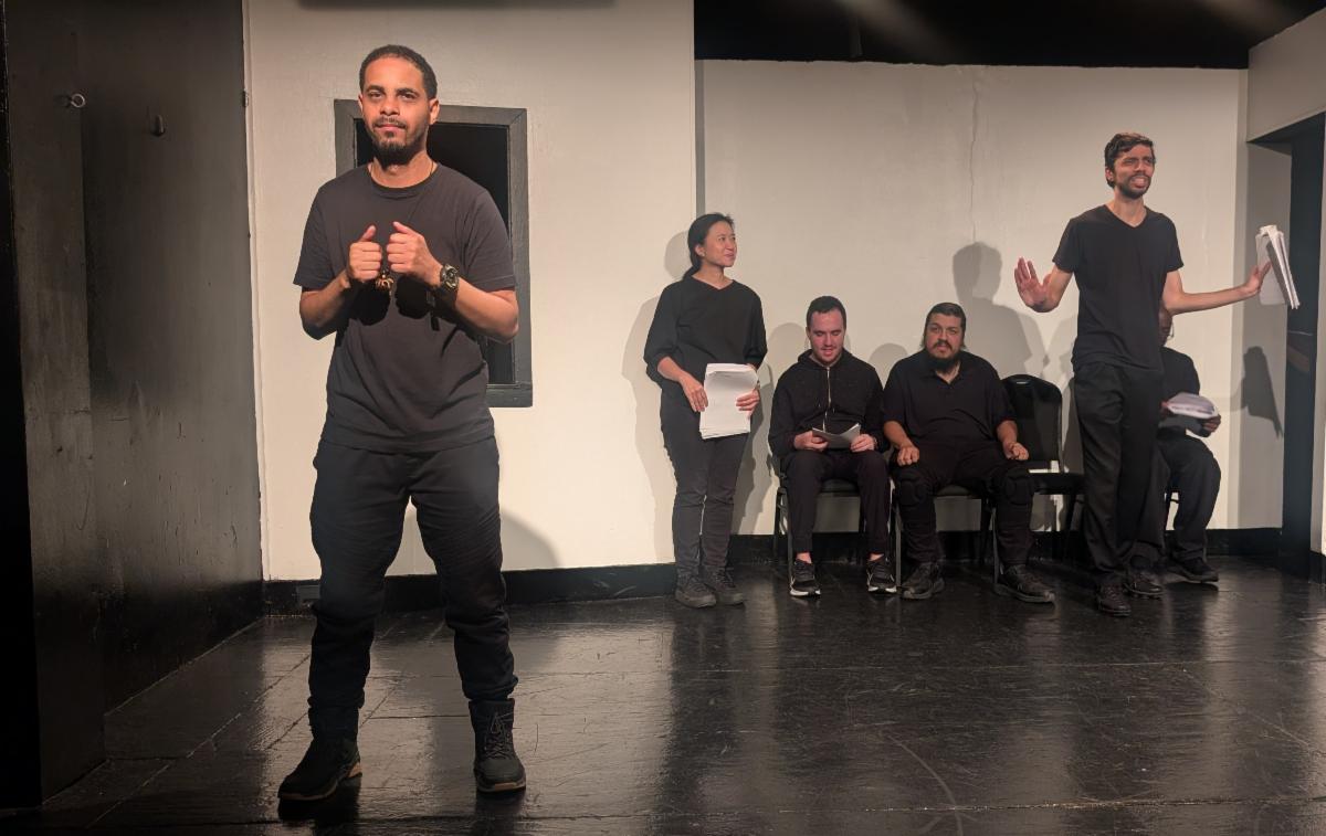 Performers wearing black hit various dramatic poses, wearing black on a black and white stage. 