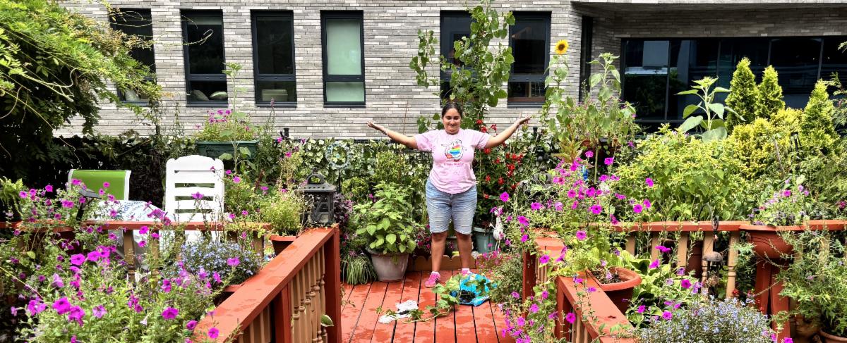 Amanda stands in a garden with her arms spread wide over pink flowers 
