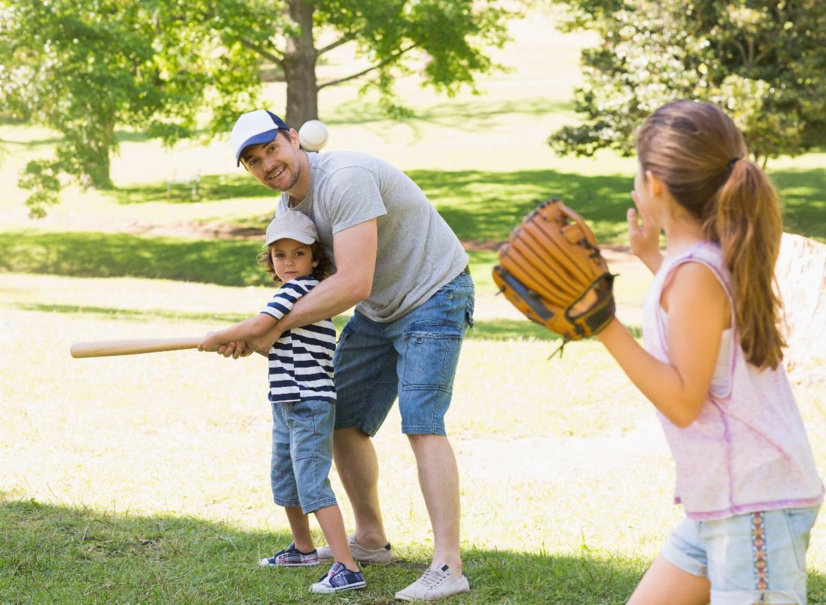 Image of a young family playing baseball in a park.