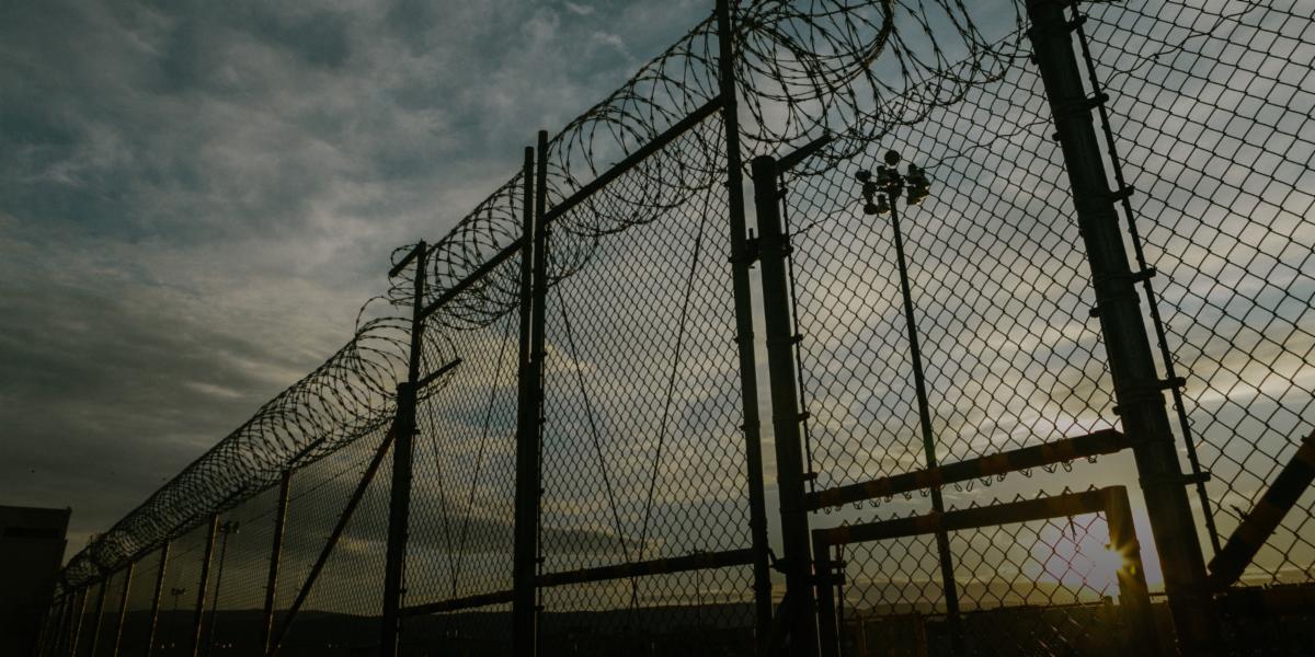 Cloudy skies in the background with a tall fence that has barbed wire at the top. 