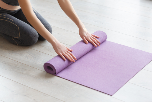 Young yoga Woman rolling her lilac mat after a yoga class on wooden floor near a window_ close up