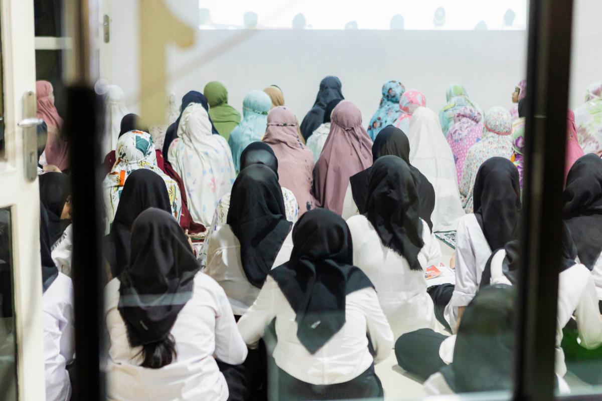 Group of Indonesian women wearing hijabs sitting on the floor and attentively listening to a speaker during a conference fostering community and promoting education and learning together