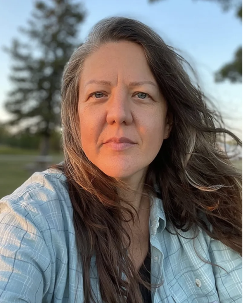 Lisa Fink photo at sunset. Lisa has long brown hair and blue eyes and is wearing a light blue plaid shirt