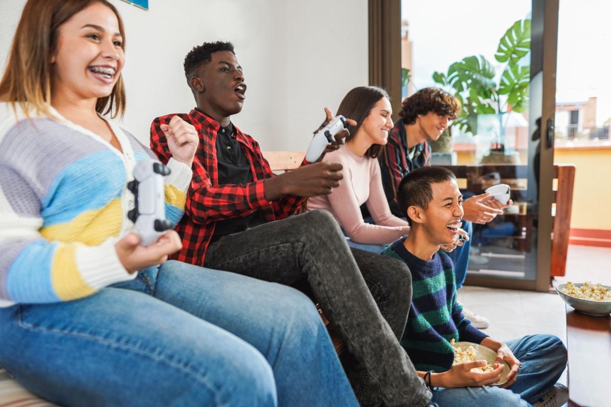 Group of five teenagers seated playing video games together.