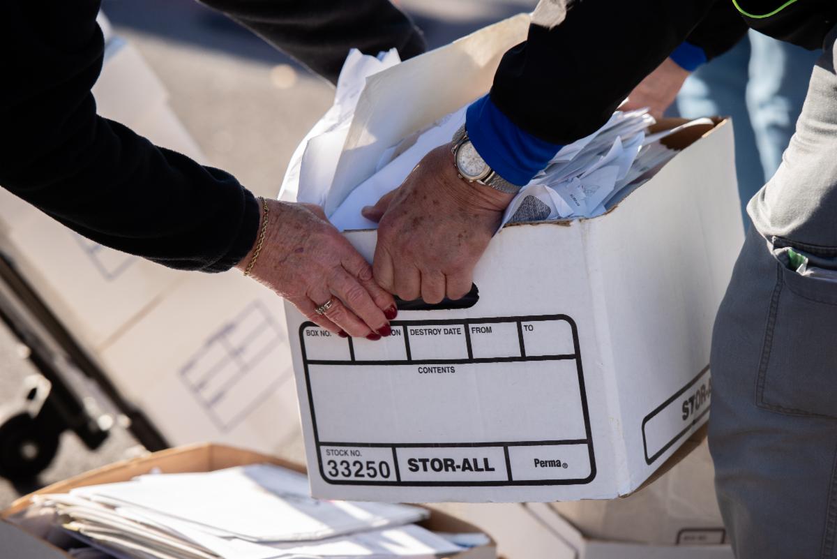 Two hands holding a cardbox box filled with papers.