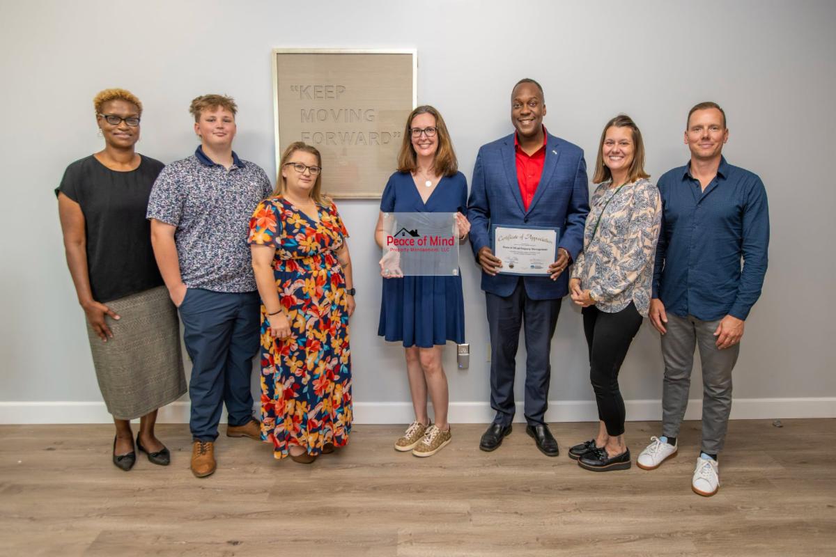 A photo of Calvin Ball and Jennifer Jones posing with the staff at Peace of Mind Property Management.