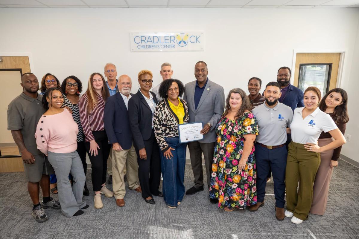 County Executive Calvin Ball posed for a photo inside Cradlerock Children's Center with its staff members and Board of Directors and Howard County Economic Development Authority CEO Jennifer Jones.