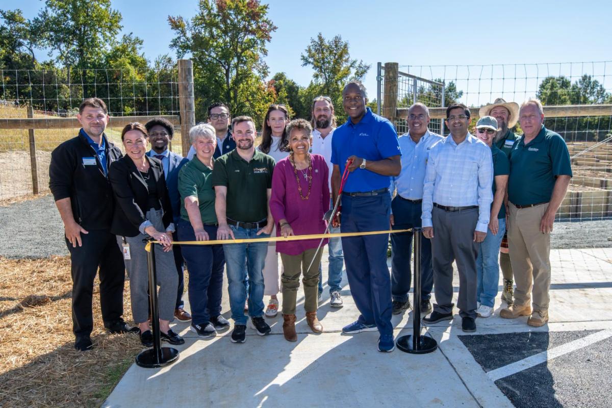 A photo of Calvin Ball posing with scissors, along with a large group, in front of a ribbon for the grand opening of the Montgomery Rd Community Garden plot
