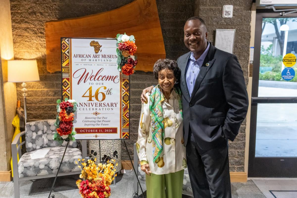 County Executive Calvin Ball posed with African Art Museum of Maryland founder Doris H. Ligon in front of a sign welcoming visitors to the museumâ€™s 46th anniversary celebration.