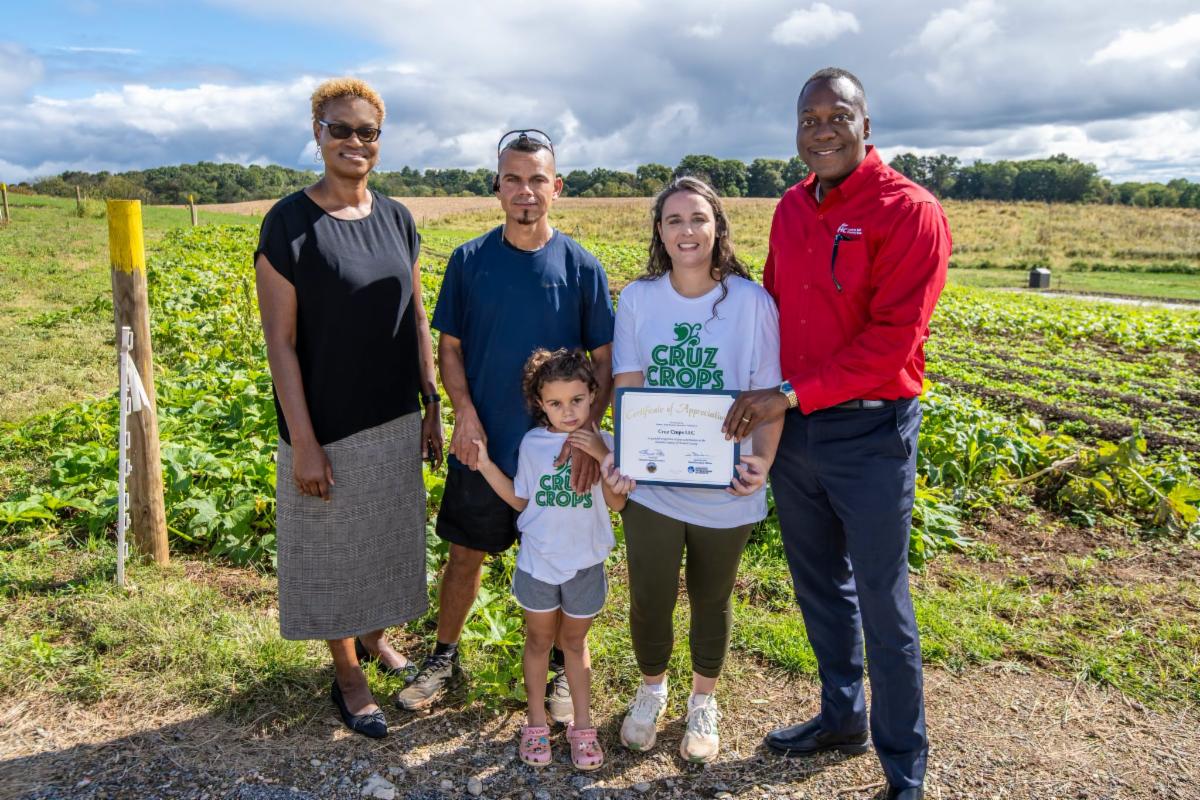 A photo of Calvin Ball and Jennifer Jones posing with Cruz Crops farmers outside on their farm..