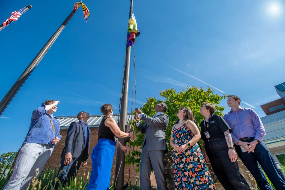 County Executive Calvin Ball and Councilperson Christiana Rigby hosting up the Pride Flag on the Howard County Flag pole surrounded by onlookers to mark the start of Pride Month in Howard County.