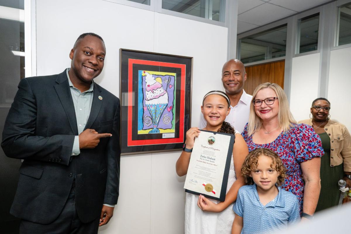 County Executive Calvin Ball posed with a student artist and their family in front of their artwork inside of the Office of the County Executive at the County's annual student art celebration.