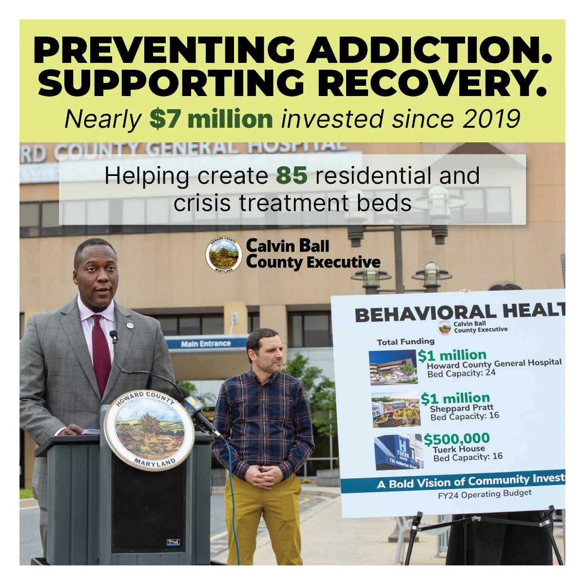 Graphic with photo of County Executive Calvin Ball speaking at a podium out front of Johns Hopkins Howard County Medical Center & text about the County's $7 million investment in behavioral health since 2019, creating 85 residential & crisis treatment beds
