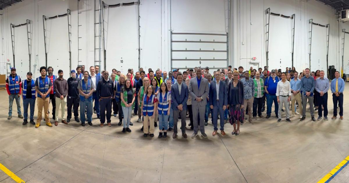 A panoramic photo of Calvin Ball posing with the staff of First Source Electronics