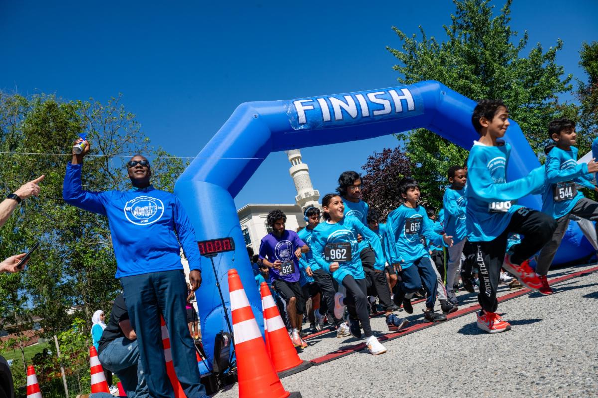 County Executive Calvin Ball blowing the start horn to the side of the start and finish blow up marker for the Islamic Society of Baltimore 2nd Annual 5K Eid Run & Walk as participants run off as the event starts.