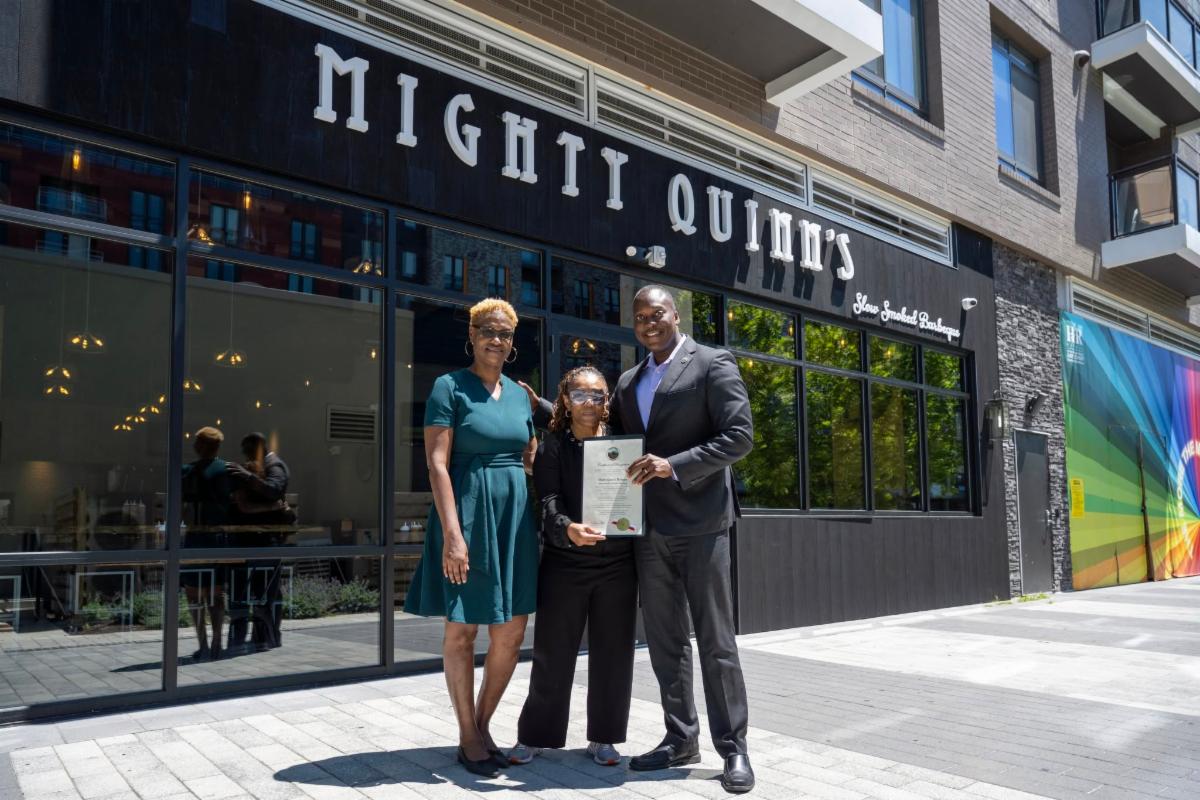 County Executive Calvin Ball posed for a photo with Mighty Quinn's BBQ franchise owner Sasha Gatling and Howard County Economic Development Authority CEO Jennifer Jones outside the restaurants new location in Columbia Maryland.