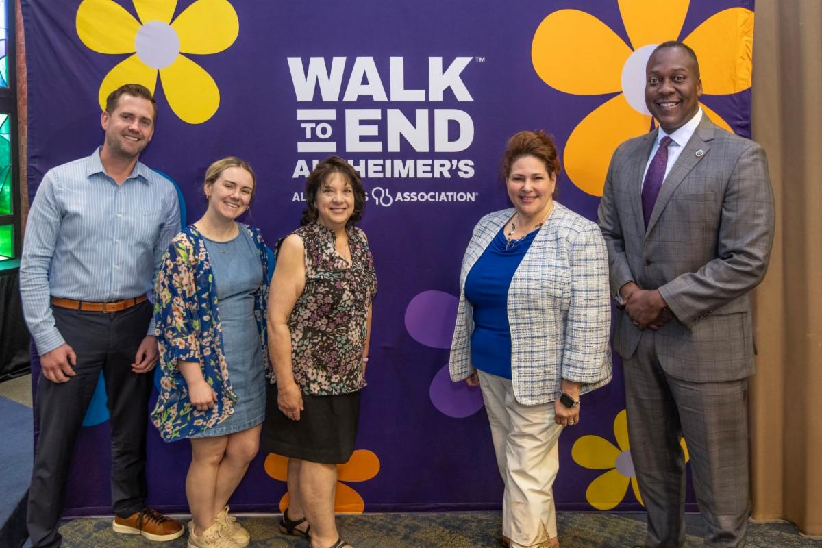 County Executive Calvin Ball posed for a photo with County Department of Community Resources and Services staff members in front of the purple Walk to End Alzheimer's step and repeat at the Alzheimerâs Association Corporate Leadership Breakfast.