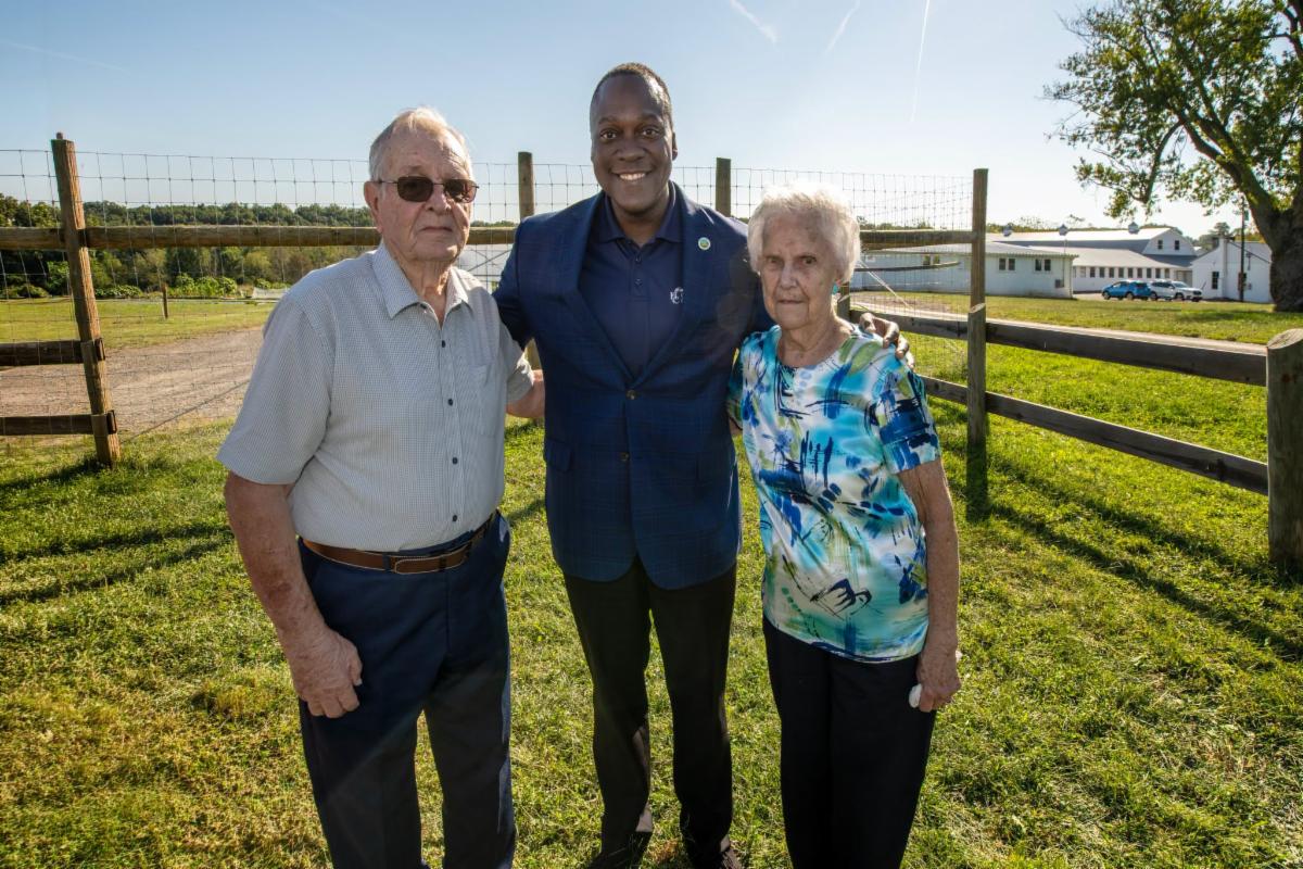 A photo of Calvin Ball posing with two farmers on their farm.