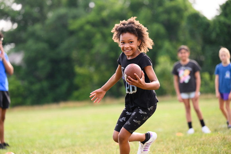 A young child running with a football in hand.