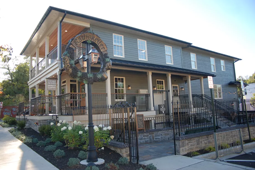 Outside of the German restaurant Rathskeller in Elkridge. A gray stone base and gray siding two story structure with a double-decker or stacked front porch.