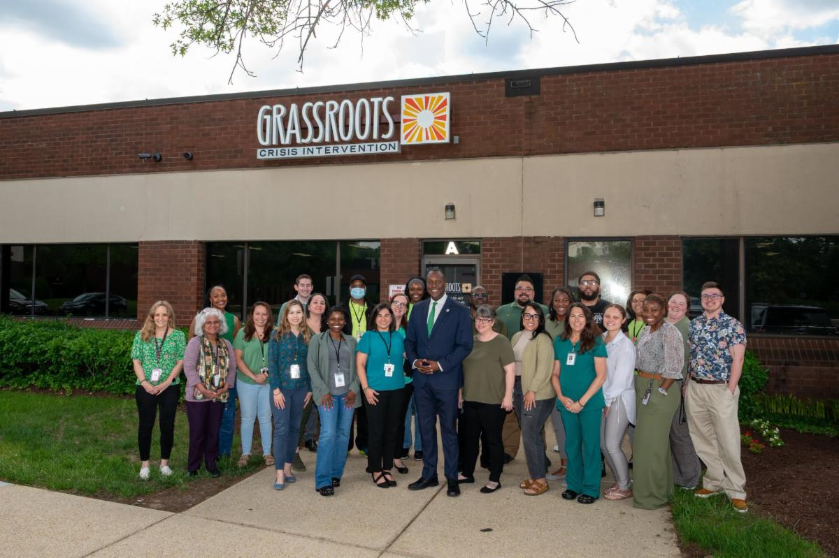 A photo of Calvin Ball posing with the staff of Grassroots, outside of the Grassroots building.