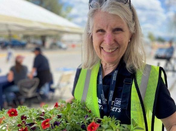 A Master Gardener carrying a tray of green plant starts with red flowers.