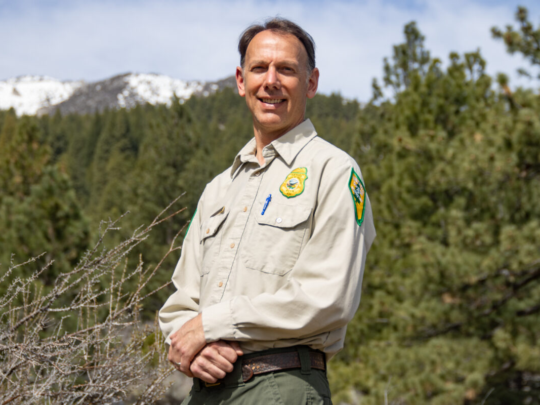 Ryan smiling in his Nevada state forester uniform with mountains and trees in the background. 