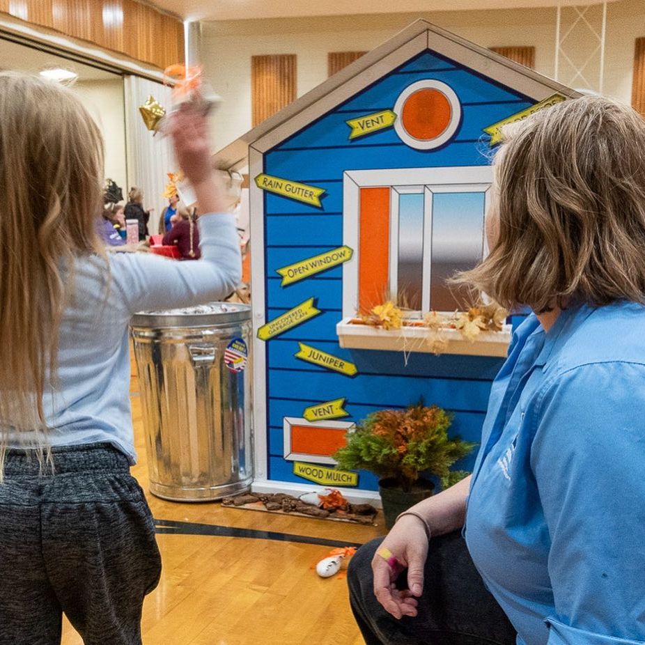 A young girl throws ember bean bags at a play house, to find out where the house is vulnerable to wildfire.