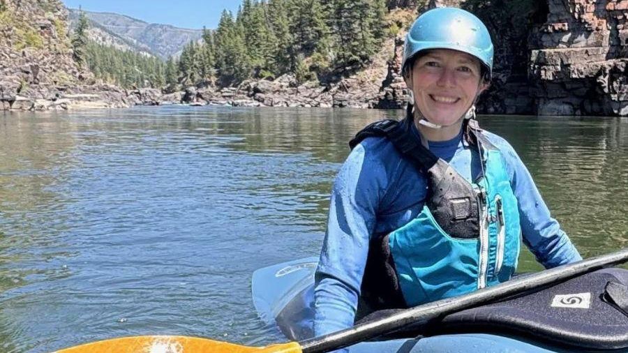 A woman in a blue helmet and lifejacket paddling a blue kayak.