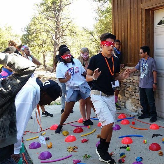 A blindfolded youth navigate an obstacle course of colorful fun toys verbally guided by their peers.