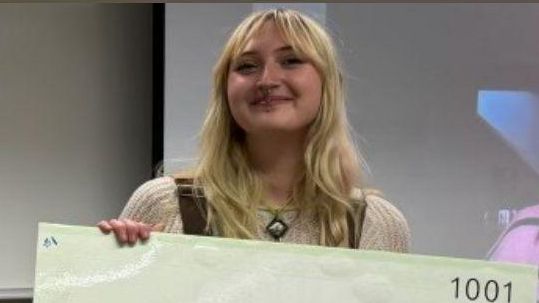 Paige holding a large check for three thousand five hundred dollars.