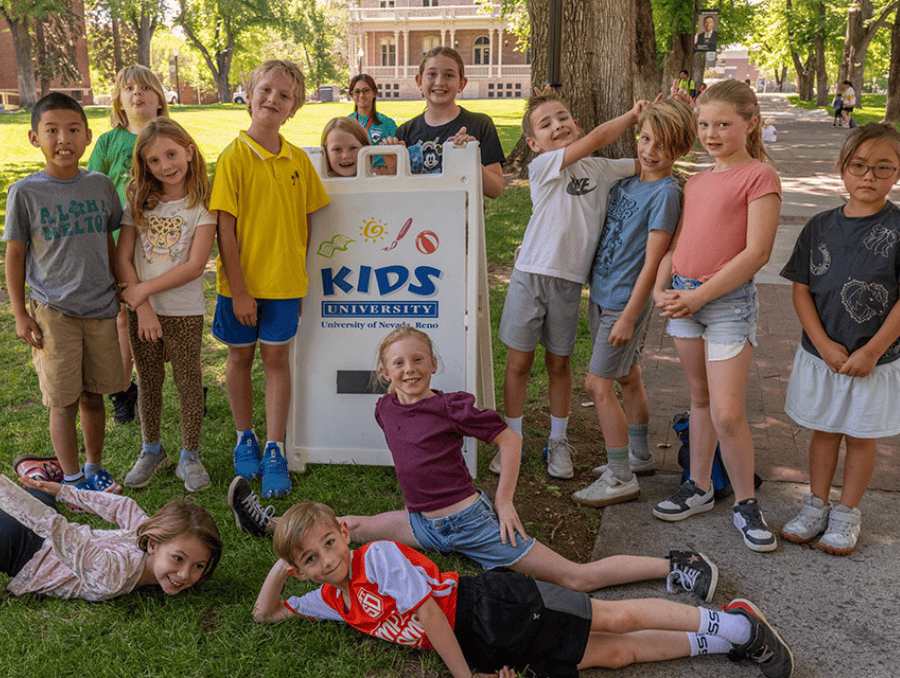A group of children standing next to a KIDS University sign. 