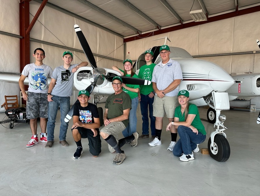 4-H youth and adults posing in front of a small plane. 