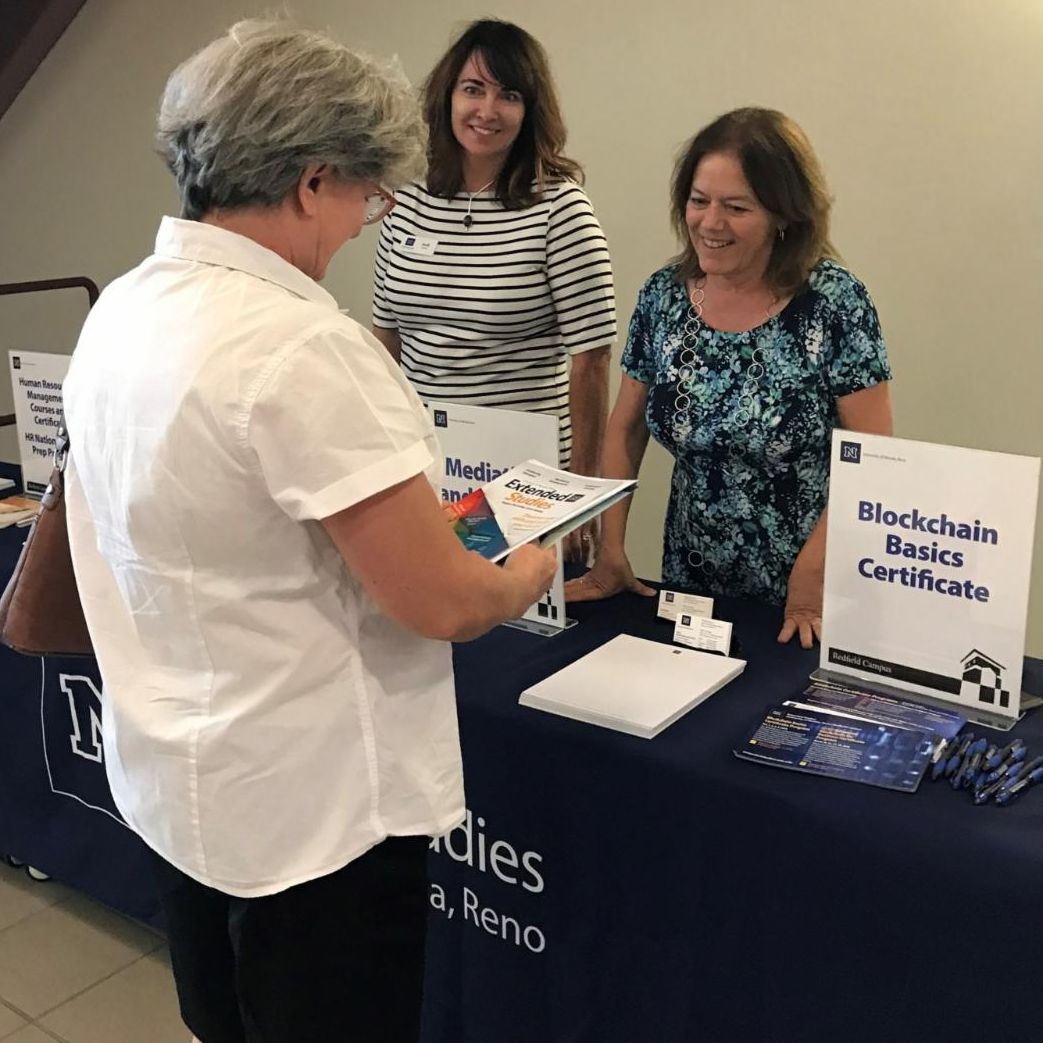 A woman receiving professional development brochures from our College's Extended Studies booth.