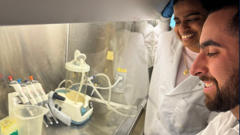 A man and woman in white overall coats observing a petri dish.