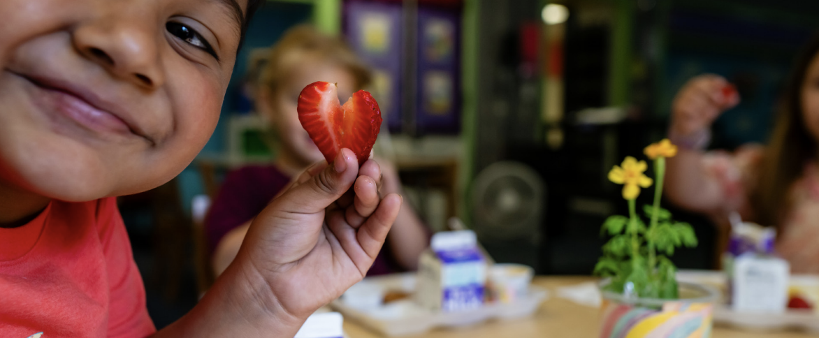 Kid holds up strawberry in shape of a heart