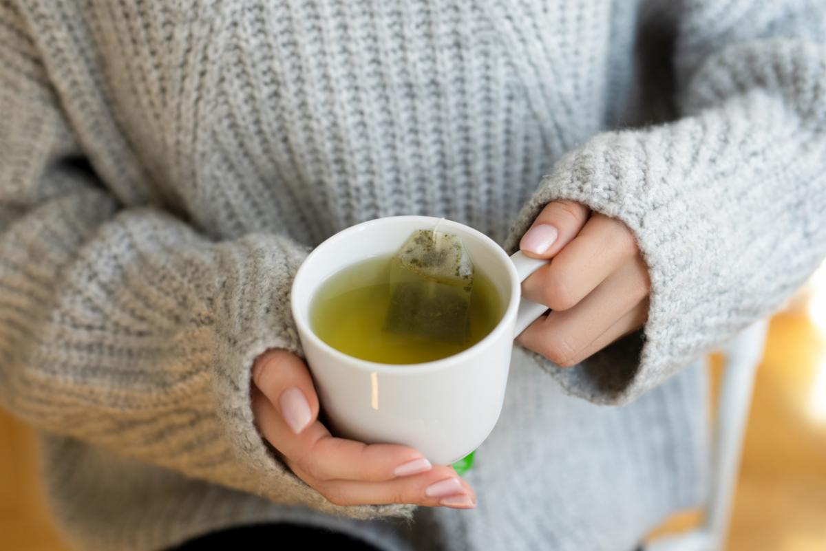 person wearing cozy sweater holding a cup of tea