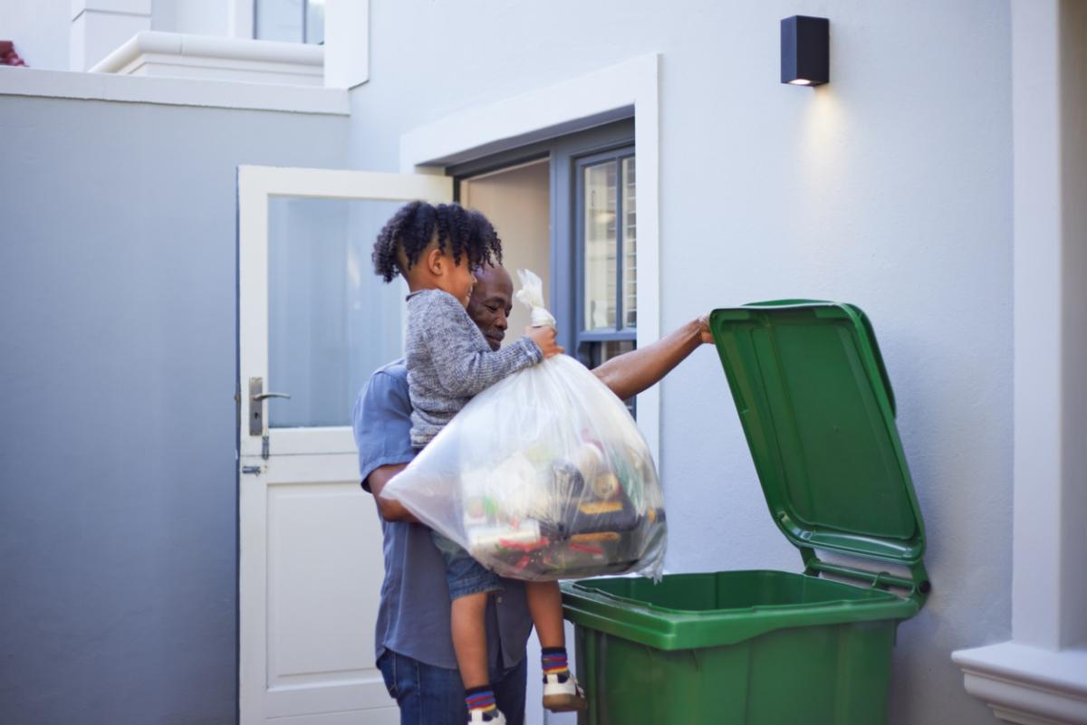 A heartwarming moment as a young boy is carried by his father or grandfather while helping take out the garbage or recycling.