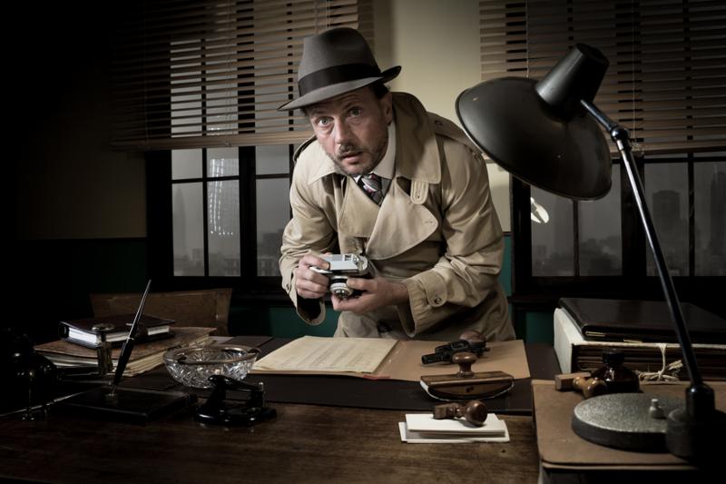 Retro spy agent caught photographing important documents on office desk 1950s style.