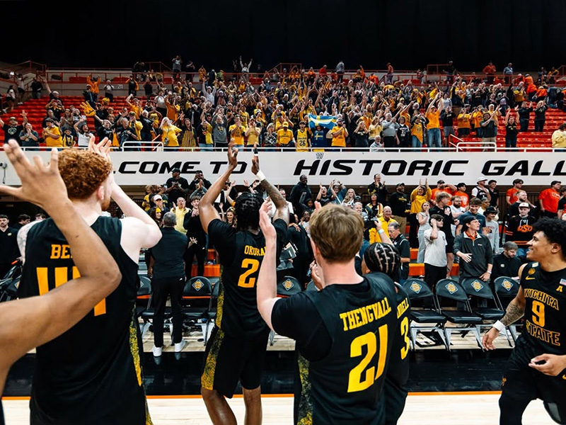 The Shocker men's basketball team in the foreground cheer alongside Wichita State fans in the crowd after the team wins its second game in the NIT