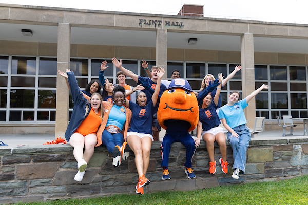 a group of students sitting with Otto the Orange mascot on a stone ledge in front of the residence hall Flint Hall